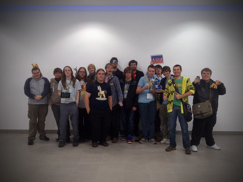 A group of 15 bronies pose in front of a plain white wall.