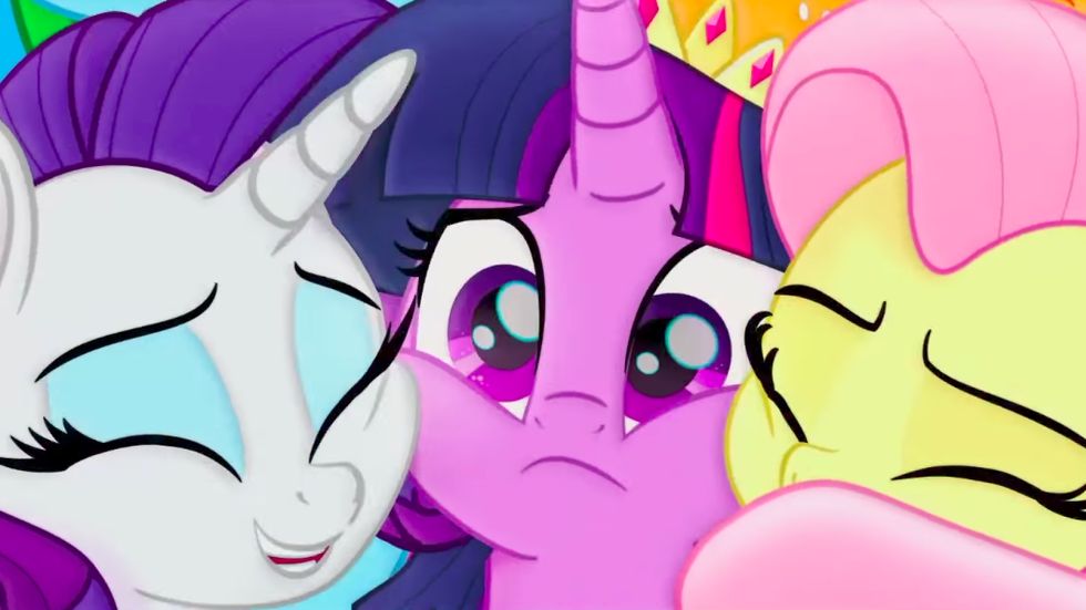 A screenshot from My Little Pony: The Movie. Rarity and Fluttershy happily hug Twilight Sparkle, however Twilight seems to be worried by something.