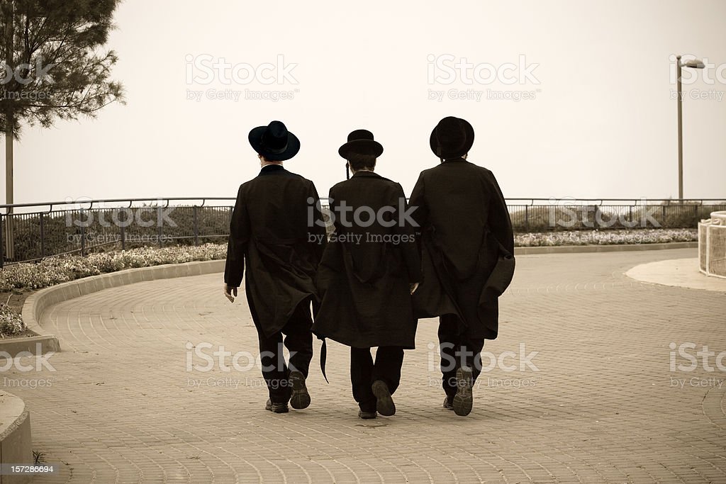 A sepia toned photo of three Hasidic Jews walking down a road together, with the iStockPhoto watermark on it.